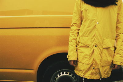 Midsection of woman wearing yellow raincoat standing against wet car