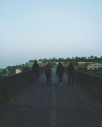 Rear view of men walking on landscape against clear sky