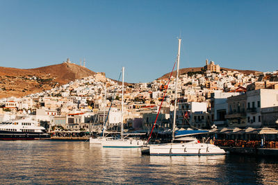 Sailboats in city by river against clear sky