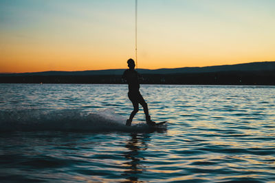 Silhouette of a man doing wakeboarding in a lake with mountains in the background