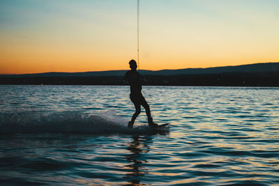 Silhouette man standing in sea against sky during sunset