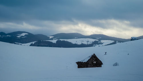 An old derelict hut in snow with cloudy sky, paltinis area, sibiu county, romania