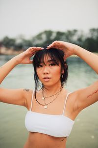 Portrait of young woman wearing bikini standing against sea and clear sky