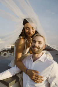 Smiling young woman with bride in wedding dress while sitting on rooftop