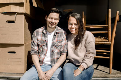 Portrait of smiling couple sitting in back of delivery truck