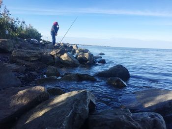 Man standing on rock by sea against sky