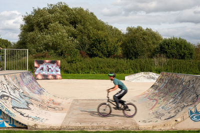 Man riding bicycle on skateboard against sky