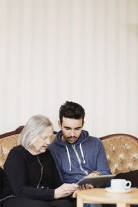 Caretaker and senior woman using digital tablet while sitting on sofa at nursing home