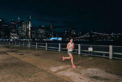 Woman running on railing against illuminated city at night