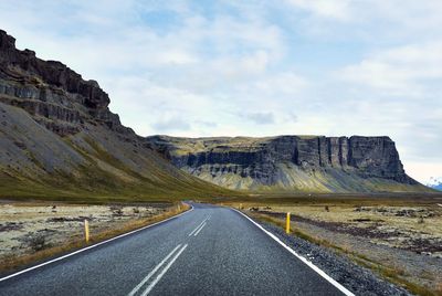 Road leading towards mountains against sky - iceland golden circle