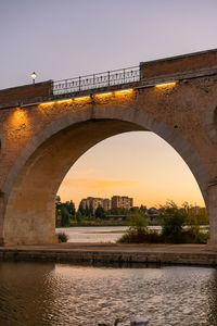 Arch bridge over river against sky during sunset