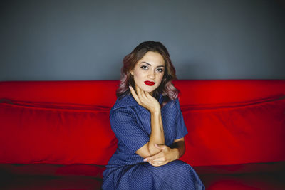 Portrait of beautiful young woman sitting on sofa against wall