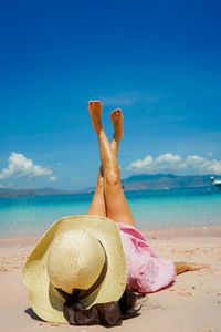 Low section of woman on beach against blue sky