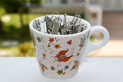 Portrait of a tiny cup filled with metal binder clips on a white surface 