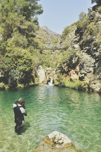 Rear view of mid adult man standing in river against sky