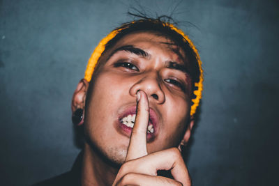 Close-up portrait of young woman gesturing silence with finger on lips at home