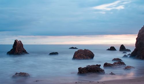 Rocks in sea against sky during sunset