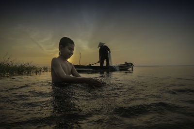 Boy swimming with man fishing in boat on sea against sky