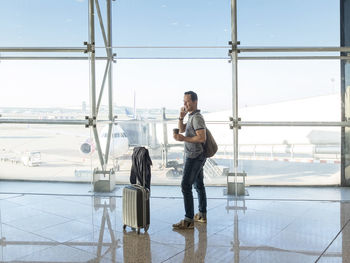 Young woman with suitcase talking on phone while waiting for flight