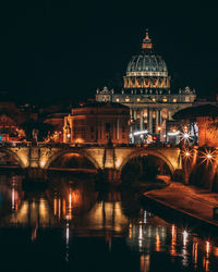 Illuminated bridge over river by buildings against sky at night