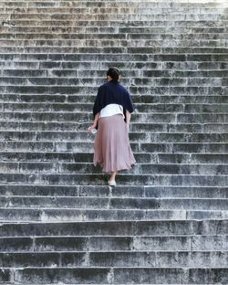 Rear view of woman standing on staircase against brick wall