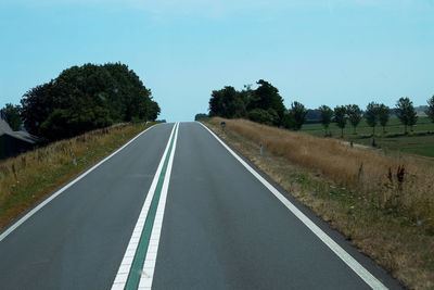 Empty road amidst trees on field against sky