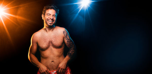 Shirtless man smiling while standing against black background