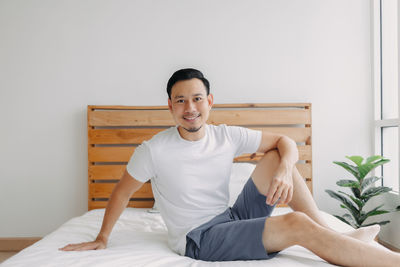 Portrait of young man sitting on bed at home