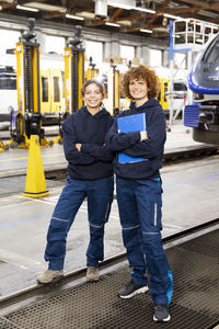 Smiling engineer holding file folder standing by colleague in manufacturing industry