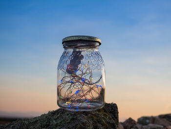 Close-up of glass jar on rock against sky