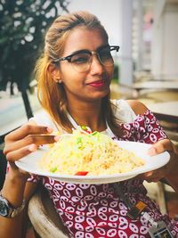 Portrait of young woman holding rice in plate while sitting on chair