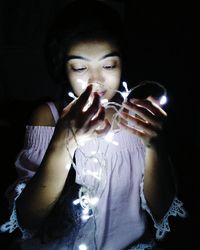 Young woman holding illuminated string lights against black background