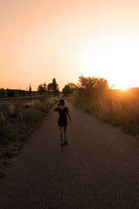 Rear view of woman walking on road against clear orange sky