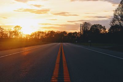 Road by silhouette trees against sky during sunset