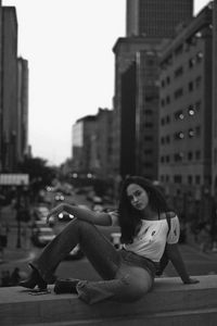 Portrait of teenage sitting on railing in city during sunset