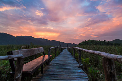 Empty boardwalk against cloudy sky during sunset