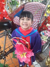 Portrait of smiling girl in graduation gown holding toy while standing at pedicab