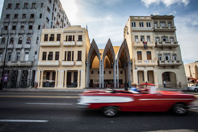 Blurred motion of red car on street against building