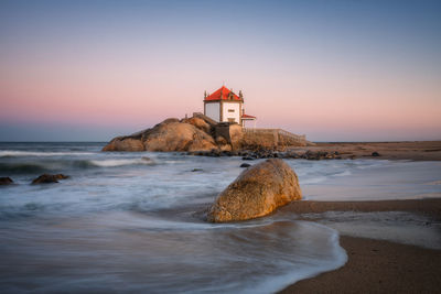 Lighthouse by sea against sky during sunset