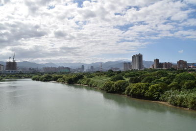 View of buildings by river against cloudy sky