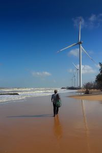 Rear view of man walking at beach against sky