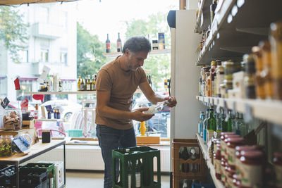 Salesman arranging bottle on shelf in deli