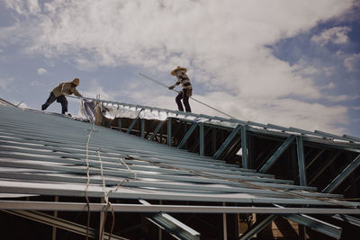 Low angle view of men working on rooftop against sky