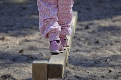 Low section of girl walking on wood over sand
