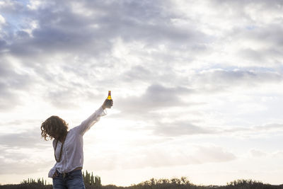 Low angle view of woman having drink against cloudy sky during sunset