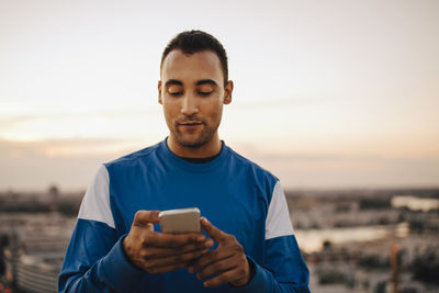 Sportsman using smart phone against sky during sunset