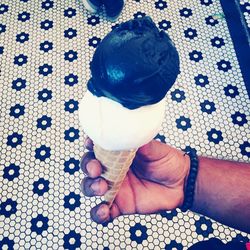 Cropped image of hand holding ice cream cone over patterned flooring