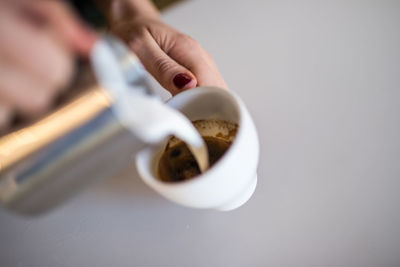 Close-up of hand pouring milk in coffee