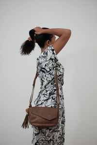 Side view of woman carrying purse while tying hair by wall