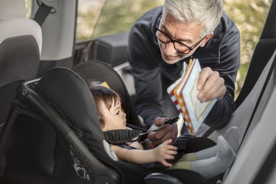 Grandfather fastening baby girl into car safety seat